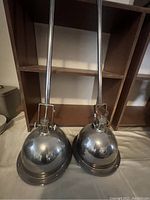 Pair of two large silver metal dome studio lights, showing the top and swivel mounting rod details.