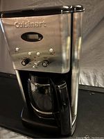 Front view of the coffee maker showing stainless steel and black plastic body with digital display and control panel.