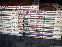 Side view of manga volumes 1-8, showing colorful character illustrations on spines, clean white backgrounds with title and author name.