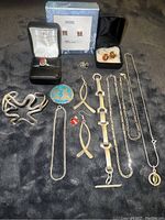 Lot contents including various pieces of silver jewelry such as a ring with a burgundy stone, multiple necklaces, earrings, cuff bracelet, and charms arranged on a black surface.