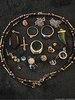 Top view showing the assortment of rings, pendants, earrings, and necklace chain spread on black cloth backdrop.