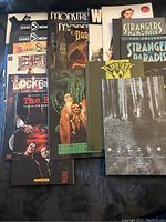 Photo showing multiple comic novels with titles visible including Snake Woman, Monstrous, Gentlemen Corpse, and others stacked on fabric background.
