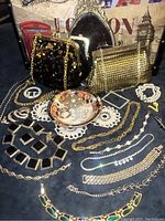 Overall lot of 2 vintage purses, assorted costume jewelry including necklaces, brooches, bracelets, rings on a dark surface with a London background.