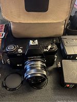 Voigtlander VSL 1 camera with attached Ultron 50mm f/1.8 lens, camera carry case, lens caps, shoulder strap, and flash unit visible on table.