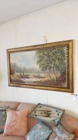 Signed framed landscape painting hung on wall above cushions