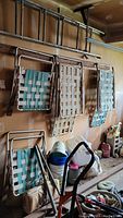 Four aluminum folding chairs with blue and white plastic webbing hanging on wall and one folded chair on floor.