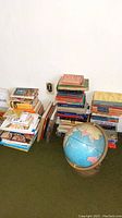 Overall view of multiple stacks of books arranged against a wall, with a globe on a metal stand placed in front of the books.