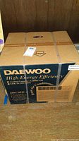 Cardboard box labeled Daewoo High Energy Efficiency Room Air Conditioner model DWC-052C, showing cooling capacity and EER ratings.