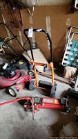 Photo showing metal adjustable hand truck with rubber wheels and a red hydraulic trolley jack beside it.