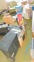 Overview photo of the lot showing Life Pro fireplace heater box and surrounding mini heaters boxed and unpacked on carpeted floor with furniture in the room