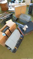 Photo of multiple stacked items showing three metal rolling carts, two vintage hard shell luggage pieces (one Starflight), a boxed item in the background, and a foldable stool.