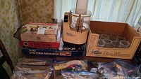 Wide view of all items together: Pyrex glass bakeware, cardboard box of glass tumblers, Moulinex food processor, apple corer and stove top grill boxes on table.