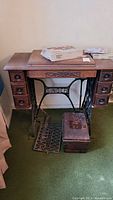 Full view of Singer electric sewing machine in wooden cabinet with foot pedal and metal case on front green carpet