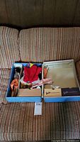 Photo showing open Barbie case containing assorted doll clothes and vintage Barbie doll wearing striped top and orange skirt.