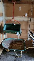 Photo of metal wheelbarrow and green Scott spreader side by side in garage