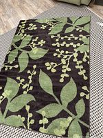 Brown rug featuring a green leaf pattern on a brown background, placed on a beige patterned floor.