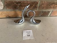 Two polished aluminum swan figurines on a brick background showing overall condition and size.