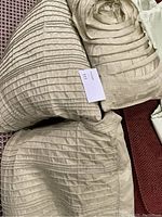 Three green cushions with a satin pleated design on a red patterned surface, two large euro sham pillows and one smaller decorative cushion.