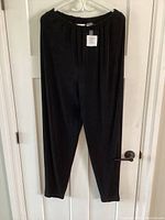 Full view of black slinky polyester pants hanging on white ornate hanger, showing shape and length.