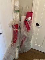 Four standing fabric bolts wrapped partially in plastic against a white door. Two white satin bolts, one red chiffon bolt, and one fuchsia linen-look satin bolt visible.