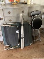 Coleman camp cot folded with tent poles bundle and folding stool next to it, showing fabric and frame condition