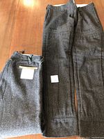 Two pairs of dark gray chainsaw protective pants laid flat, showing overall design and fabric texture.