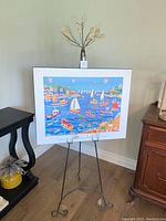 Decorative metal art easel holding the colorful Sunday Sailing print depicting sailboats and coastal houses.