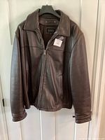 Front view of Men’s brown leather coat, size XL hanging on a hanger against a white door.