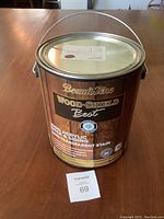 A photo of a metal can of Beauti-Tone Wood Shield Best 100% acrylic deck and siding semi transparent stain on a wooden table.