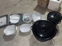 Corningware glass bakeware dishes with lids and black roasting pots with lids on basement floor