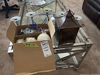 Wide shot showing all items on glass table including the candelabra, lantern, and box of candles.