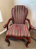 Front view of dark stained wooden armchair with wingback design and striped fabric upholstery in red, gold, and brown tones.