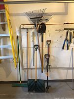 Full view of the garden tools hung on pegboard including broom, rakes, shovels, and garden fork