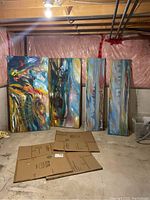 Four large abstract acrylic paintings leaning against a wall in a basement, cardboard boxes on floor, canvases vary in size two large, two narrow and tall