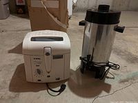 Both T-Fal deep fryer and coffee percolator shown side by side on concrete floor in basement.