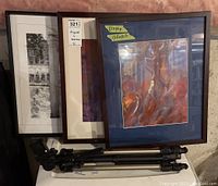 Photo showing three framed art pieces leaned against a white surface with Velbon CX 440 tripod folded in front.