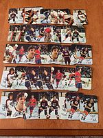 Forty 1977/78 O-Pee-Chee glossy hockey insert cards laid flat on wood surface, showing front images of NHL players with printed autographs and action/portrait shots.