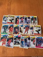 Photo shows 20 hockey cards laid out on a wooden surface, featuring multiple NHL players from 1983/84 O-Pee-Chee set.