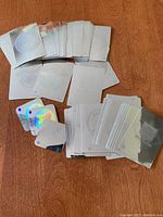 Top-down view of approximately 80 holographic baseball cards spread in groups, showing backs and some fronts. Cards feature reflective silver and holographic surfaces with MLB team logos.