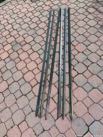 Six black metal landscape posts laid out on a paved surface.