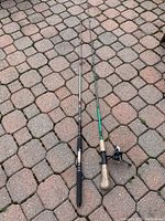 Two fishing rods lying on a paved surface, one with a black foam handle grip, the other with a cork handle grip with a reel attached.