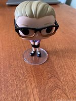 Front view of Young Harley Quinn Funko Pop with glasses and ponytail, standing on clear circular base.