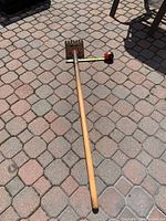 Metal roof shingle scraper remover with long wooden handle on a brick paved ground, showing full tool length.