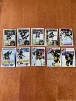 Ten vintage Boston Bruins hockey cards arranged on a wooden surface, clearly showing player images and the Bruins logo.