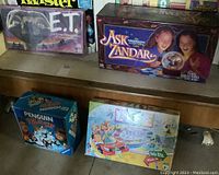 Five vintage board games stacked or displayed on a shelf: E.T., Ask Zandar, Penguin Pileup, Game of Life, and Twister. E.T. box shows wear and is missing spaceship cards as noted.