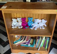 Solid wood bookshelf with dings and scratches, seven Beanie Babies on top shelf, children's books on lower shelf.