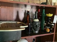 Wood bar sign on top shelf with several collectible liquor bottles on lower shelf including cat-shaped and novelty shaped bottles.