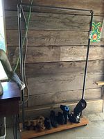 Full view of industrial metal clothes rack with wooden base, showing the frame and some shoes on the base for scale.