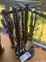 Costume jewelry necklaces hanging on black metal spinning display rack viewed from side, showing multiple colorful necklaces.