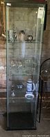 Tall glass display cabinet with black laminate top and base, shown from front with contents inside (not included in sale).